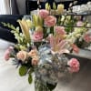Mixed arrangement of pink lilies, roses, carnations, and blue hydrangea in a clear glass vase