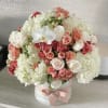 Round bouquet of white hydrangeas, pink roses, and white orchids in a white box with a pink ribbon