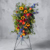 Tall standing floral spray with sunflowers, roses, and blue flowers on a metal easel