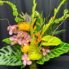 Tropical arrangement with pink orchids, yellow pincushion blooms, and anthuriums in a glass vase