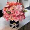 Pink and peach roses arranged in a black hat box with a ribbon