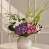 Mixed bouquet with purple hydrangea, pink roses, white lilies, and a ceramic vase