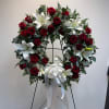 Circular wreath of red roses and white lilies on a stand with a white ribbon