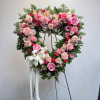 Heart-shaped pink floral wreath on a stand with a white ribbon bow