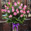 Pink roses arranged in a clear glass vase with a purple ribbon