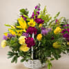 Basket arrangement of yellow lilies, purple flowers, and pink carnations