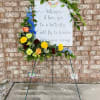 Standing floral tribute with butterflies and a memorial sign
