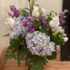 Bouquet of blue hydrangeas, white roses, and purple flowers in a glass vase