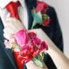 Pink rose corsage on a wrist with a matching boutonniere on a suit
