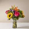 Mixed bouquet of roses, lilies, sunflowers, and purple blooms in a glass vase