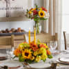 Yellow and orange floral centerpiece with two candles on a dining table
