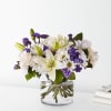 White lilies and daisies with purple filler in a clear glass vase