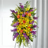 Tall standing floral spray with yellow lilies, orange roses, and purple flowers