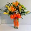 Orange lilies and green chrysanthemums in a clear glass vase with an orange ribbon