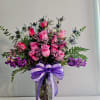 Pink and purple rose bouquet in a clear glass vase with a purple ribbon