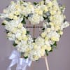 Heart-shaped white floral wreath on an easel with a ribbon bow