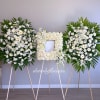 Three white floral funeral sprays on easels, with a rose frame in the center
