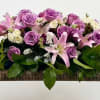 Soft lavender roses and pale pink lilies spill across a low, elongated