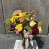 Mixed bouquet of yellow, pink, red, and cream flowers in a glass vase with a ribbon