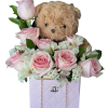 Pink roses and white flowers arranged around a teddy bear in a pink box