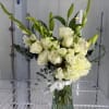 Tall arrangement of white roses, lilies, and hydrangea with green buds in a clear glass vase.