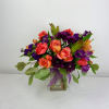 Mixed bouquet of purple, coral, and orange flowers in a glass vase