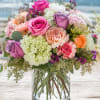 A lush, rounded bouquet of roses, hydrangeas and carnations in pink, purple