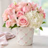 Pink roses and alstroemeria arranged in a white vase with pink bows