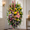 A tall oval standing spray of pink lilies, yellow chrysanthemums, and stately