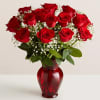 Red roses arranged in a red glass vase with baby's breath