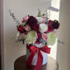 Bouquet of pink, red, white, and burgundy flowers in a white hat box with a red ribbon