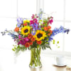 Bright mixed bouquet with sunflowers, roses, irises, and blue flowers in a glass vase