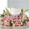 Pink roses and carnations arranged around a white urn.