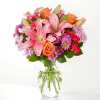 Pink lilies, orange roses, and purple daisies in a clear glass vase