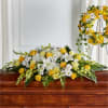 Yellow and white floral casket spray with a matching wreath on a stand