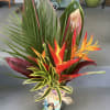Tropical arrangement with orange-red heliconia and variegated foliage in a wrapped vase