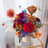 A rich and artistic floral arrangement featuring luxurious caramel roses, vibrant crimson
