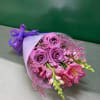 Bouquet of lavender roses and pink flowers wrapped in white paper with a purple ribbon