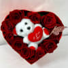Heart-shaped box of red roses with a small teddy bear holding a heart