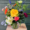 Glass container includes hydrangea, roses, veronica, gerbera daisies, mini carnations, dusty miller