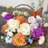 Basket arrangement of roses, daisies, and purple blooms with a butterfly accent