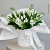 White tulips and small white flowers in a white hatbox with a ribbon