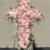 Pink floral cross on a stand with ribbon and white filler flowers