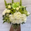 Tall white and green flower arrangement with hydrangeas and roses in a clear glass vase
