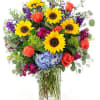 Bouquet of sunflowers, coral roses, and purple flowers in a glass vase