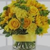 Yellow roses and sunflowers arranged in a glass vase with a yellow ribbon.