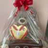 Gift basket with a teddy bear and heart-shaped chocolate box wrapped in clear plastic