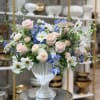 Pastel bouquet of pink roses, white daisies, and blue flowers in a white vase