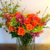 Orange roses and purple orchids in a clear glass vase