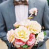 Man holding a bouquet of pale pink and cream roses with a boutonniere on his jacket